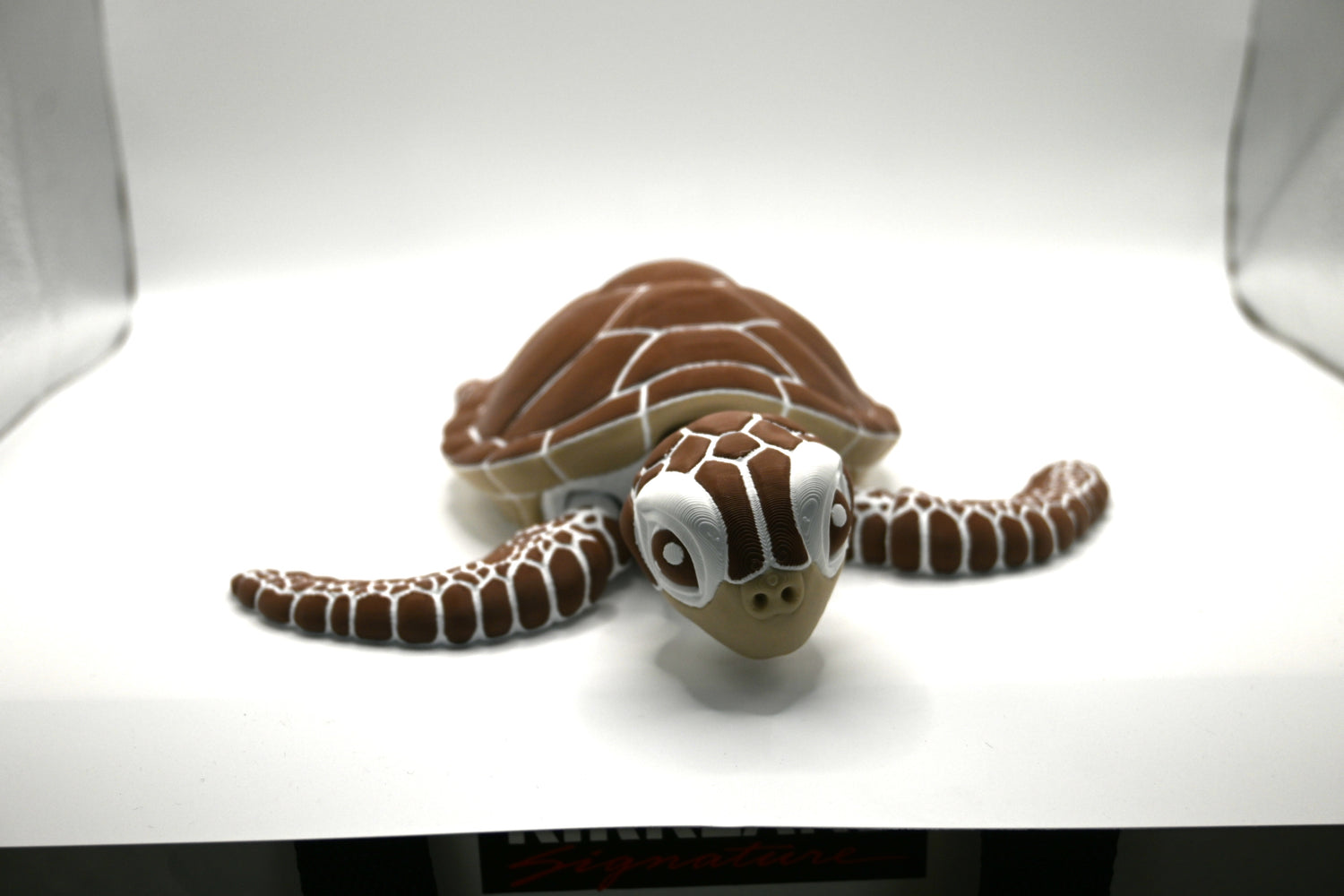Brown and white toy sea turtle lying flat on a white background, showcasing its detailed design.